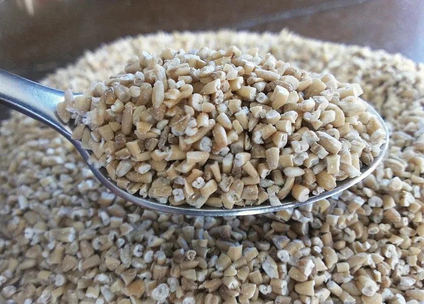 Dry pinhead oats in a spoon above a bowl of oats